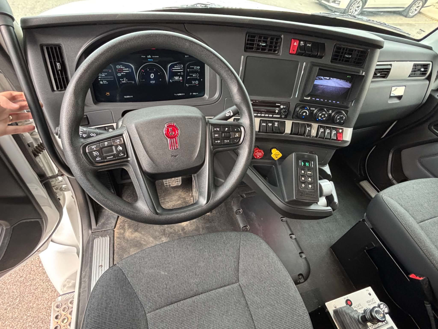 Kenworth T880 interior dashboard and steering wheel showing digital gauges, center console with controls, gear selector, and steering wheel with red emblem.