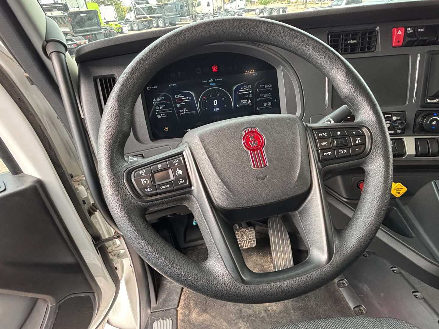 Kenworth T880 truck interior dashboard and steering wheel with digital instrument cluster visible. Steering wheel center shows Kenworth emblem. Various control buttons on steering wheel and dashboard panel.