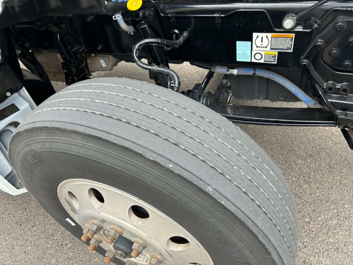 Kenworth T880 wheel and suspension area showing front dual rear tires, with hydraulic lines and chassis markings visible.