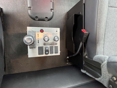 Kenworth T880 interior console panel showing control switches and gauges, including a small round knob and a rectangular control panel with labels like UP, DOWN, and ROAD FORCED. Some text visible: THROTTLE? HANDLE? and multiple black push-