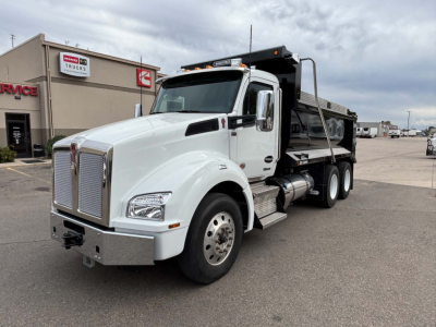 Kenworth T880 dump truck in white cab with black dump bed, front-left angle, chrome grille and bumper, diesel exhaust and side steps visible.