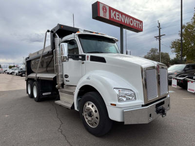 Kenworth T880 dump truck in service bay showing front grille, large chrome bumper, side exhaust, and dump bed under clear sky.
