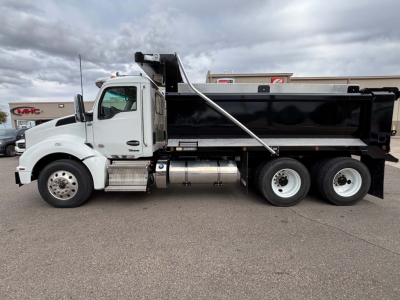 Kenworth T880 dump truck side view showing black dump body, white cab, chrome fuel tanks, dual rear axles, and front axle with wheel.