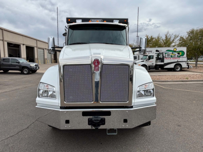 Kenworth T880 front view showing large chrome grille, bumper, and headlights. Silver truck with chrome mirrors and center Kenworth emblem.