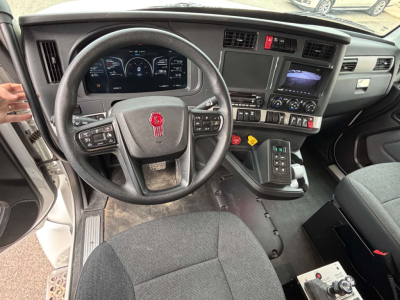 Kenworth T880 interior dashboard and steering wheel showing digital gauges, center console with controls, gear selector, and steering wheel with red emblem.