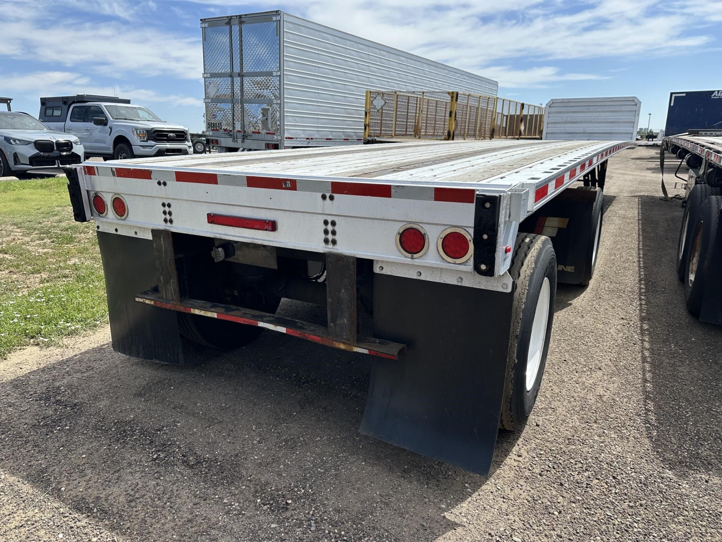 Flatbed trailer rear view showing dual axles and mud flaps with reflective tape and taillights.