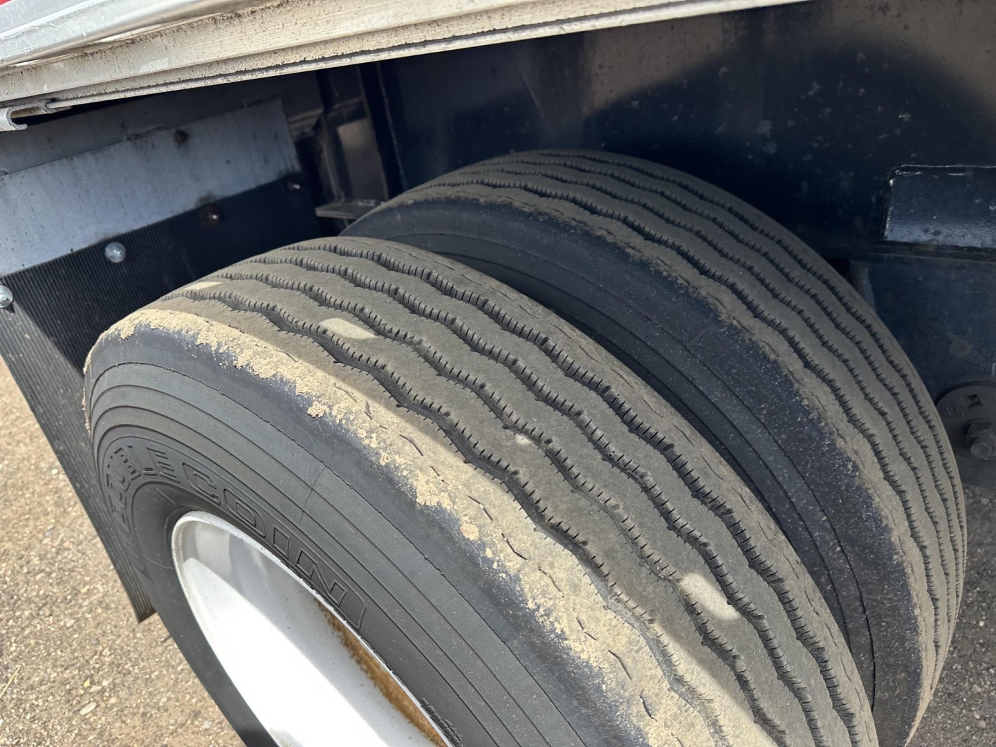 Flatbed trailer wheel and tire close-up showing dual tires with tread and a sand-colored dust on the sidewall; Fontaine Infinity trailer component visible