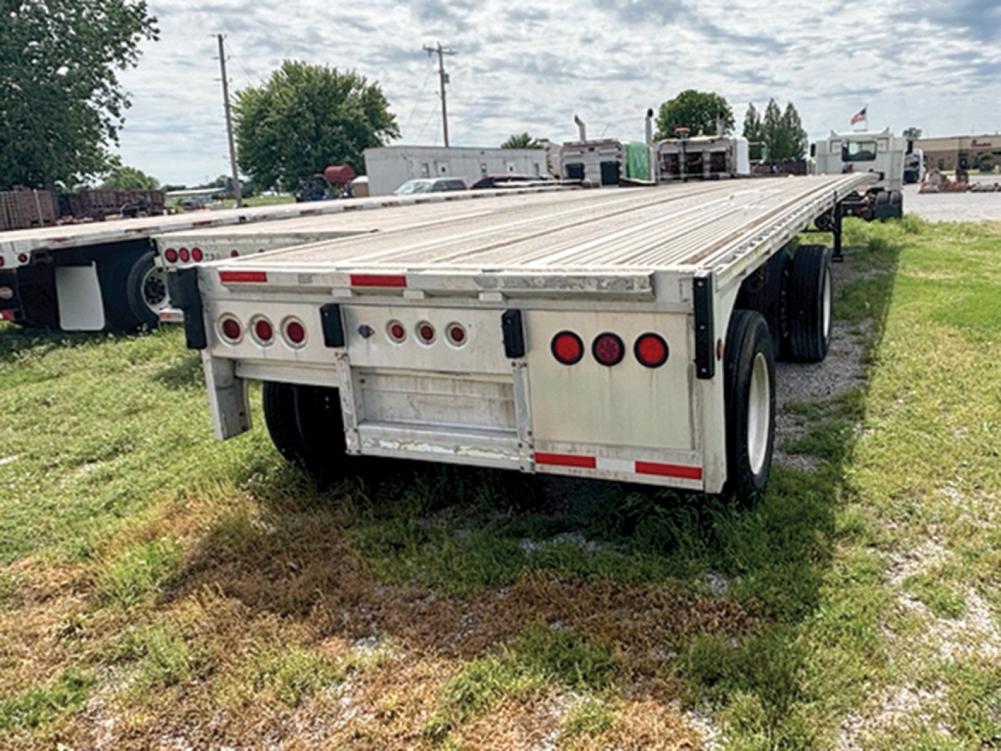 Flatbed trailer rear view with multiple taillights and metal deck showing Reitnouer MaxMiser branding not visible. Textured aluminum side rails and dual rear axles.