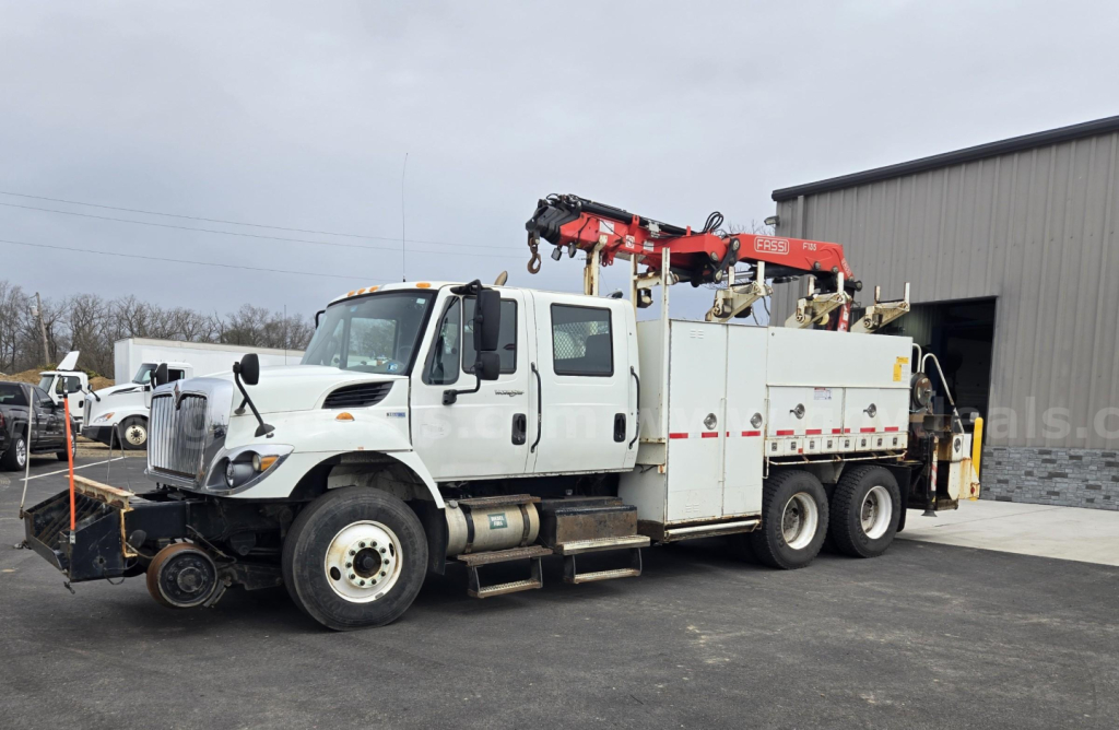 2015 International WorkStar tow truck with mounted crane and utility compartments in a yard.
