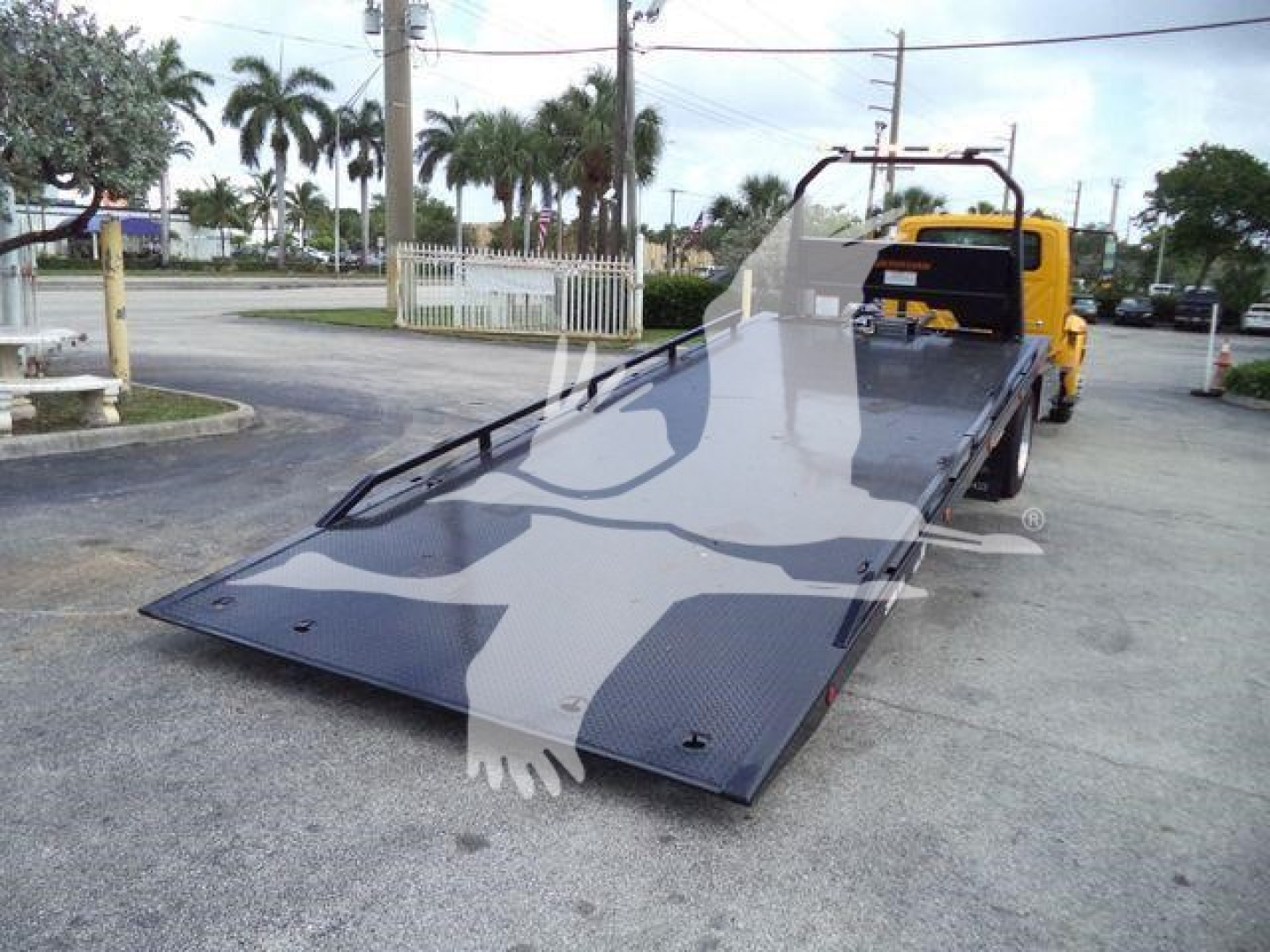 Flatbed tow truck bed with hydraulic tilt and a yellow cab in background.