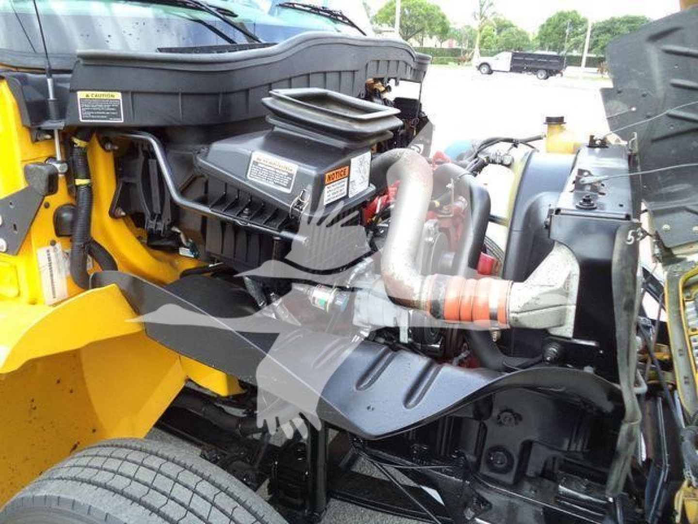 Truck engine bay of a 2019 International 4300 rollback showing engine components, hoses, and surrounding yellow bodywork.