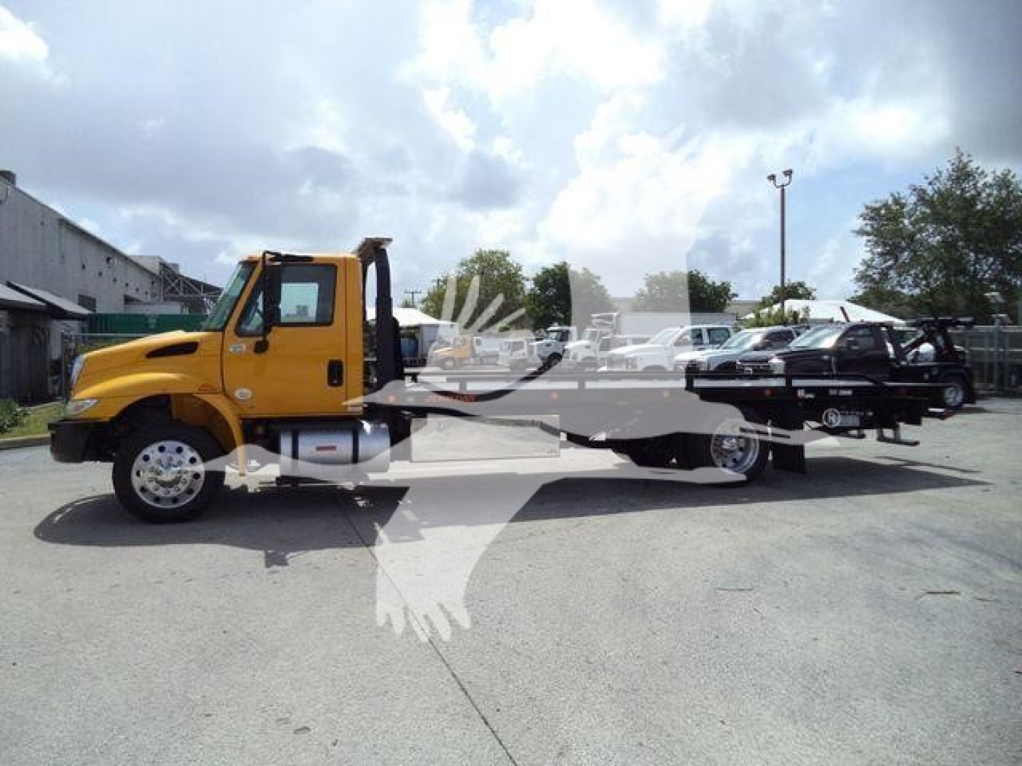 Yellow 2019 International 4300 rollback tow truck in a lot, flatbed with black trucks loaded on rear, stock number T12255FM.