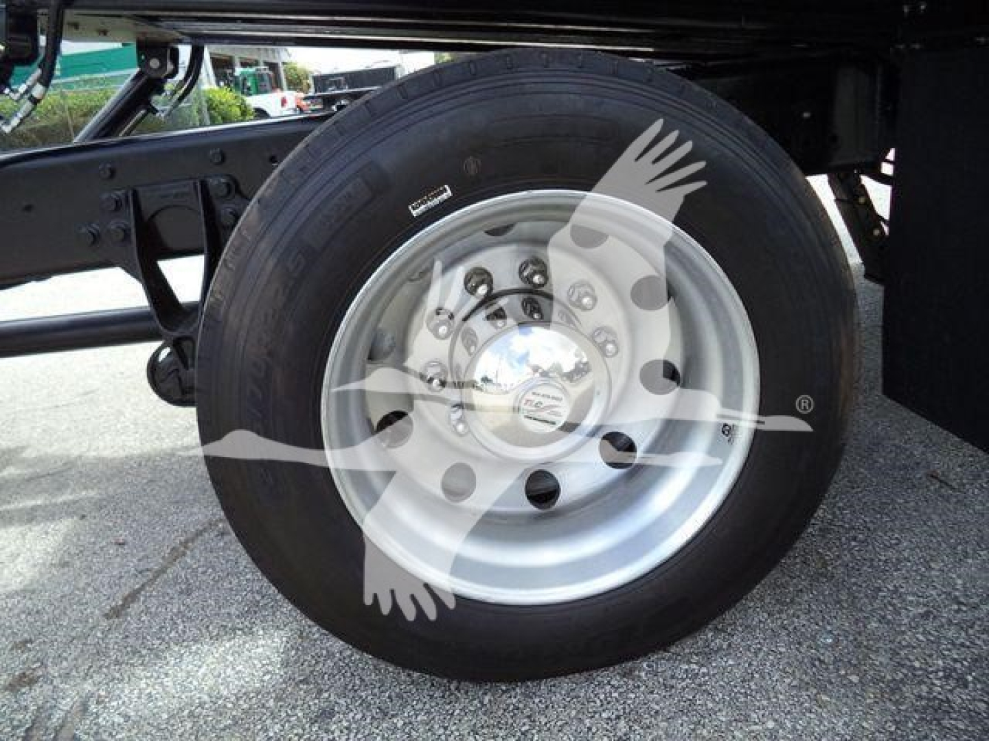 Truck wheel and dual rear axle area showing a silver steel wheel with lug nuts and a large black tire, undercarriage supports visible.
