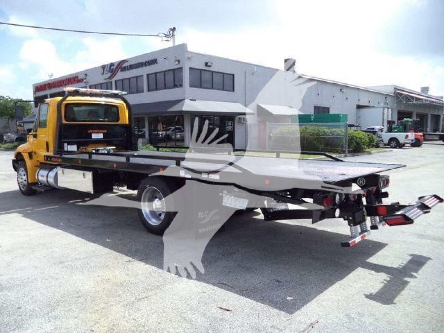 Flatbed tow truck with yellow cab and black lowboy bed in a dealership lot, International 4300 model, rear view showing ramps and towing equipment.
