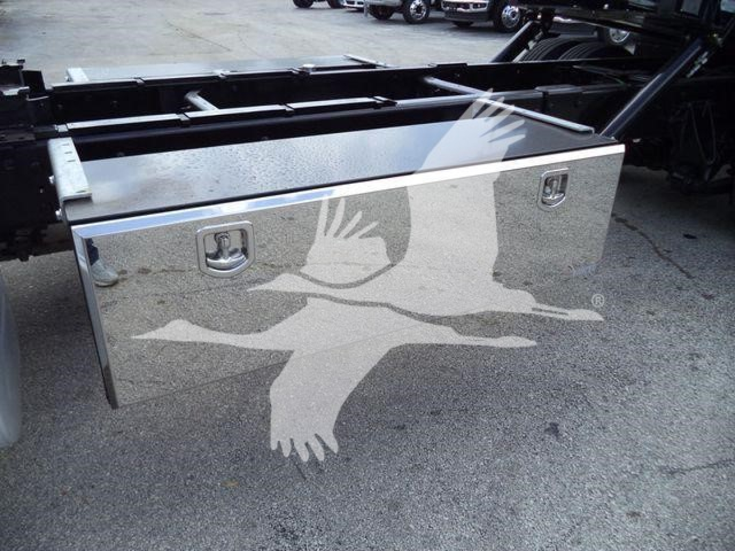 Toolbox/storage box mounted on truck chassis with handles and reflective surface, side view.