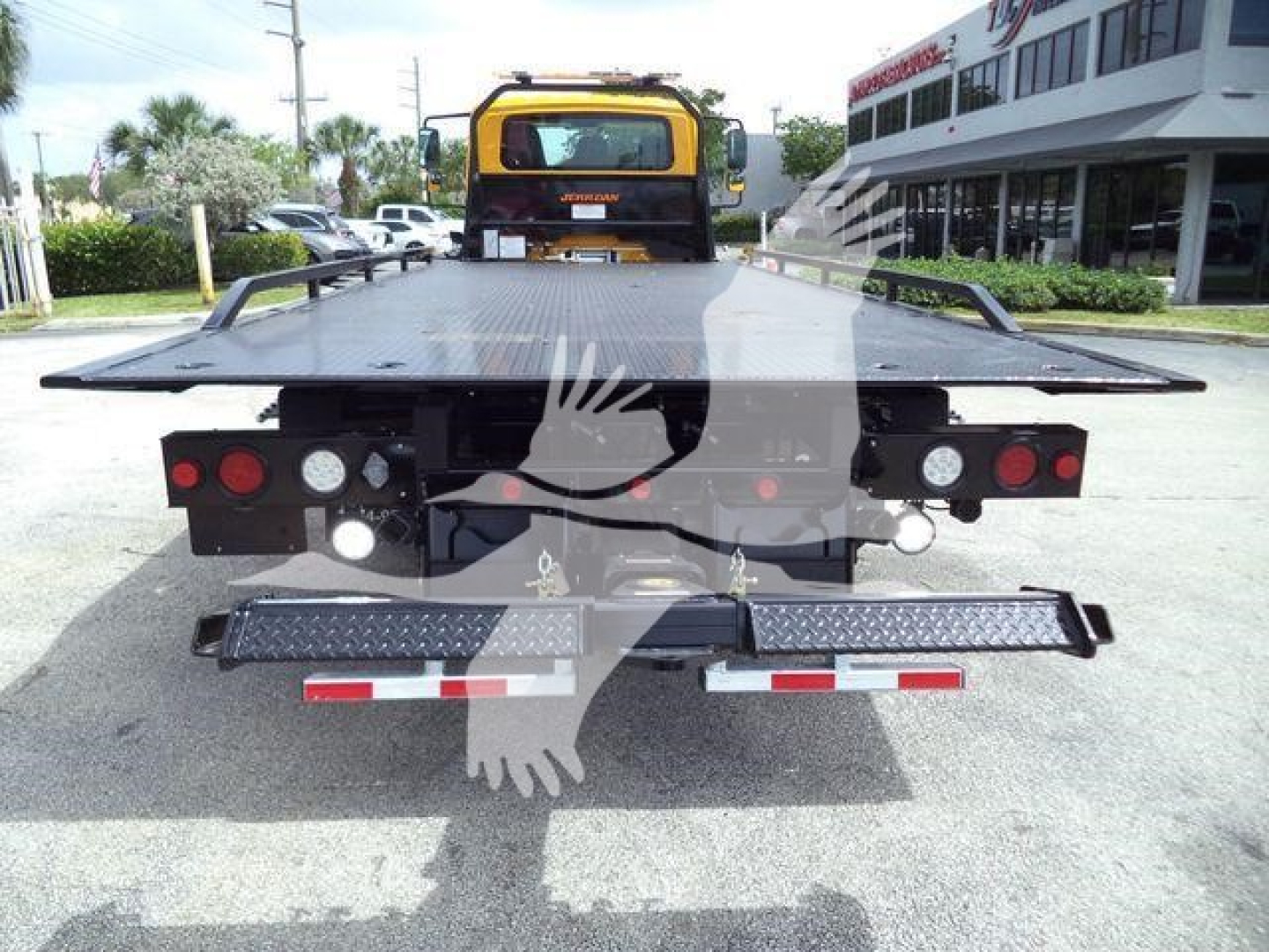Back view of a rollback tow truck with a flatbed, rear lights, and bumper steps. Visible text includes on the site watermarked photo; no legible serials or labels readable on the truck.