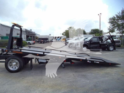 Flatbed rollback tow truck attached to rollback trailer with hydraulic ramps and wheel lift, side view.