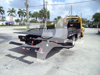 2019 International 4300 rollback truck with flatbed viewed from rear-left in a parking lot.