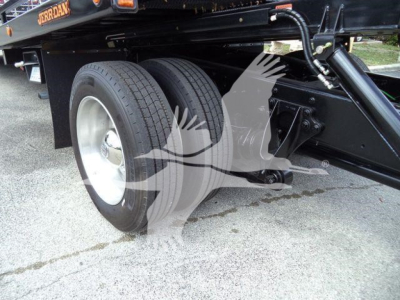 Dual rear wheels on a rollback tow truck chassis with black frame and hydraulic components visible.
