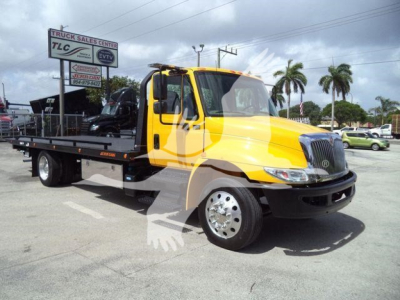 Yellow 2019 International 4300 rollback tow truck seen from side angle with flatbed and crane accessories, stock number T12255FM visible in background.