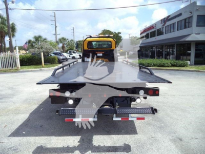 Truck bed of a rollback tow truck with yellow cab, rear view showing flatbed and taillights.