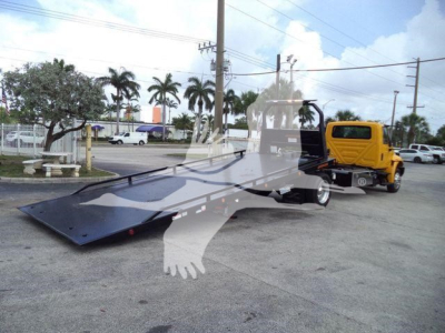 Flatbed tow truck with a yellow cab and black/deck bed, viewed from side, in a dealership lot.