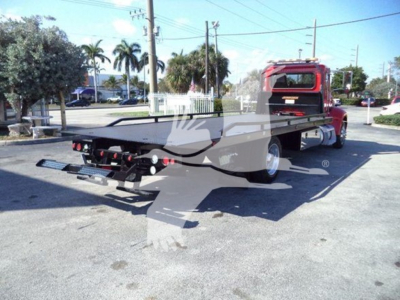 Peterbilt 337 rollback tow truck rear view showing flatbed and rear bumper with hitch, red cab, suburban lot background.