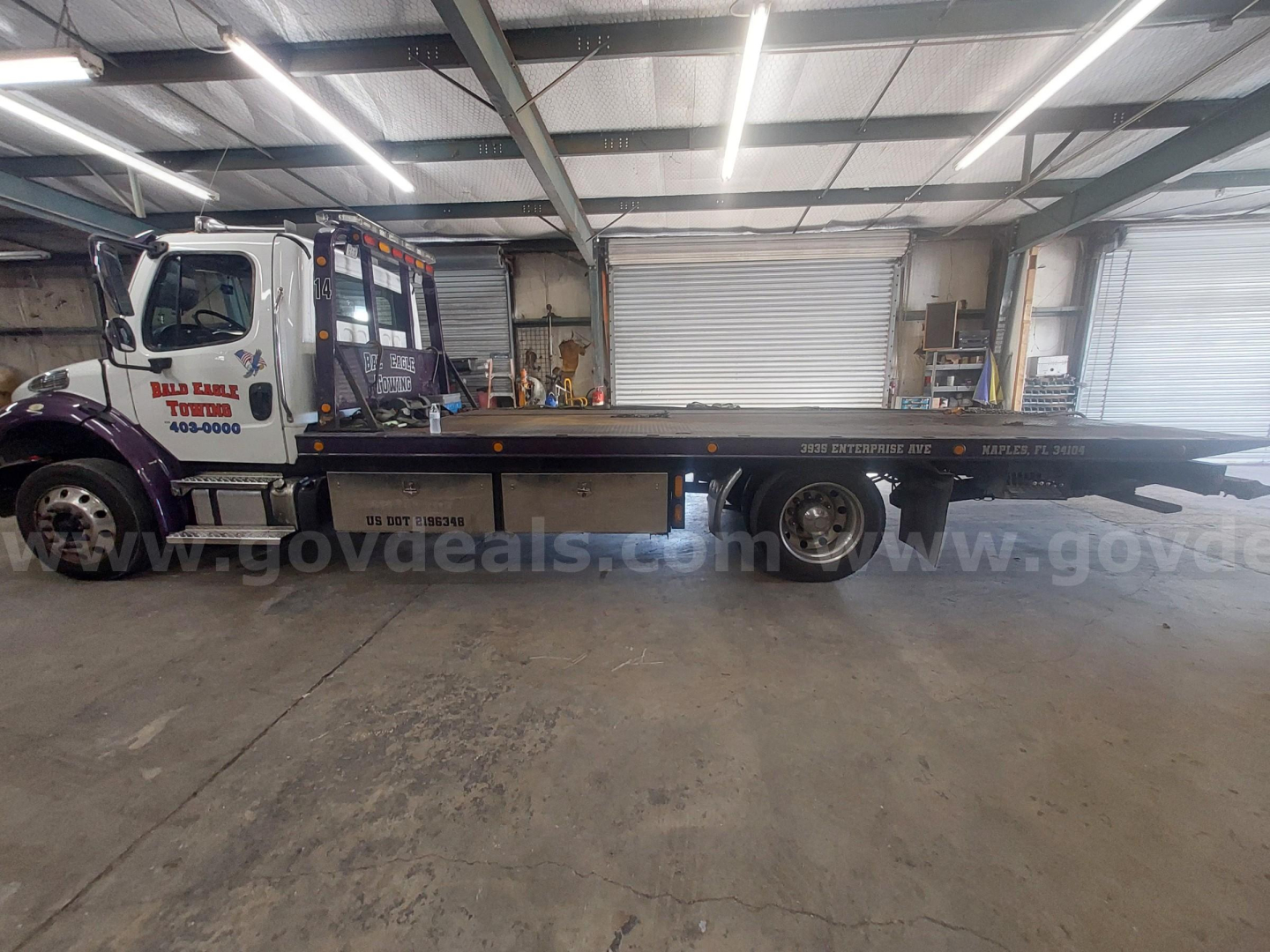 Truck cab and flatbed tow truck in a warehouse showing Freightliner M2 with long flatbed