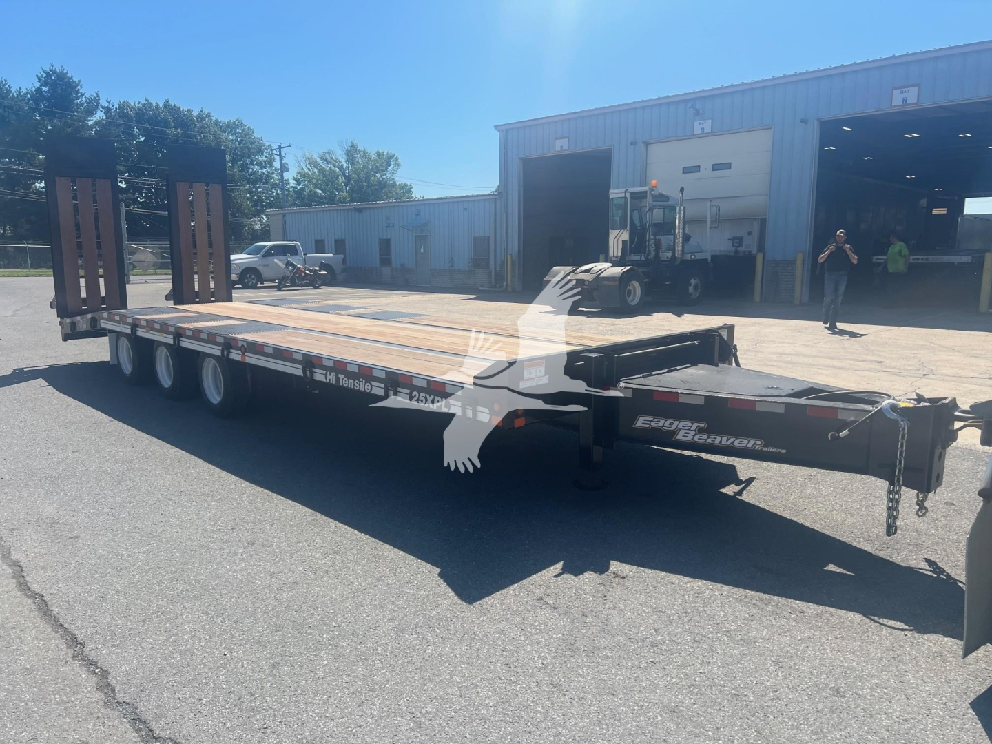 Trailer deck of a 2026 Eager Beaver 25XPL flatbed trailer viewed from side showing gooseneck, tandem axles, and ramps; branding 'Eager Beaver' and Stiles Trucks near front.
