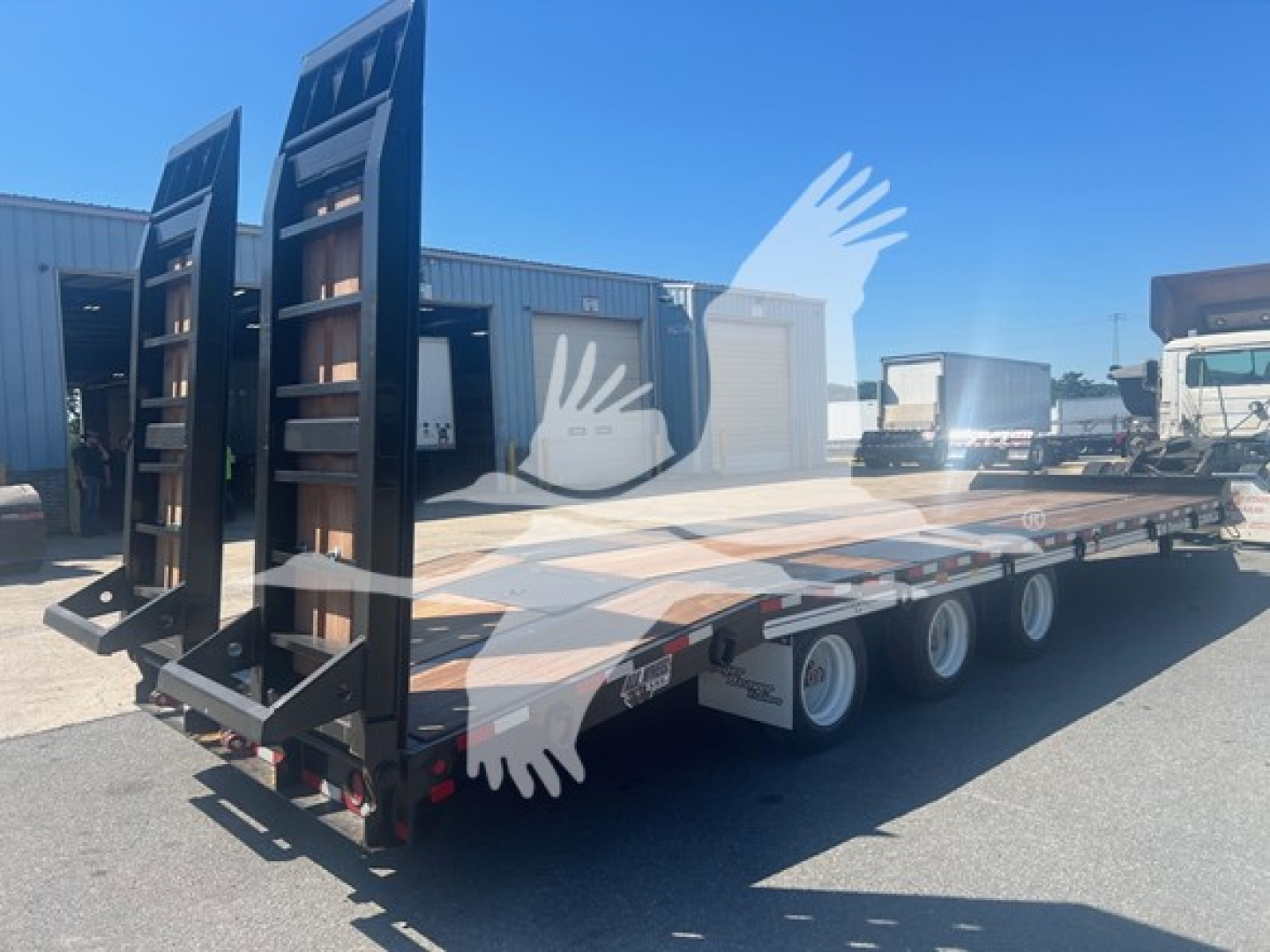 Trailer deck showing dual tandems with black ramps and hydraulic deck system, 3-axle trailer with white wheels and side markers.