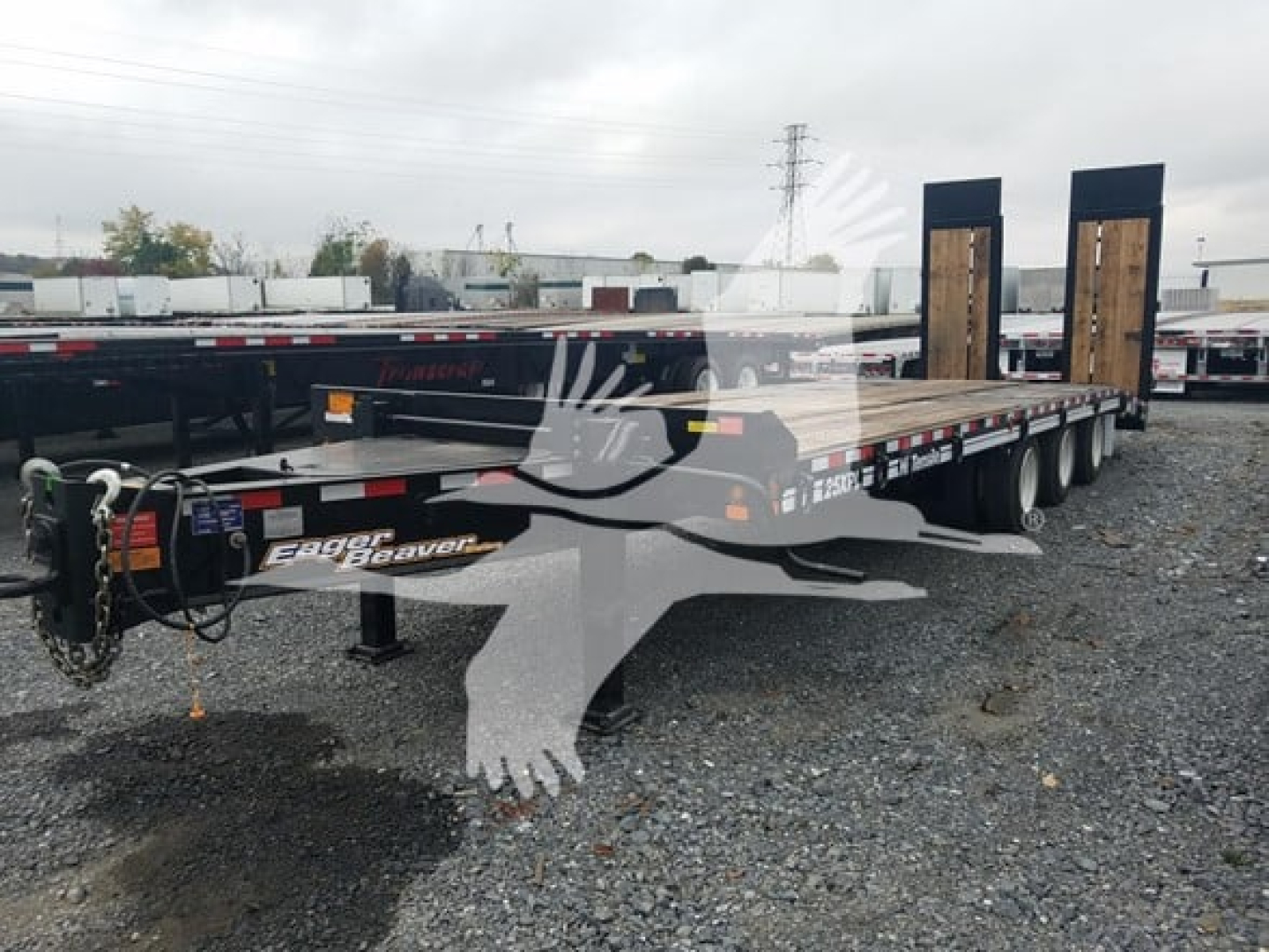 Flatbed trailer showing dual axles and goose-neck style front with ramps up, brand 'Eager Beaver' decals visible on side.