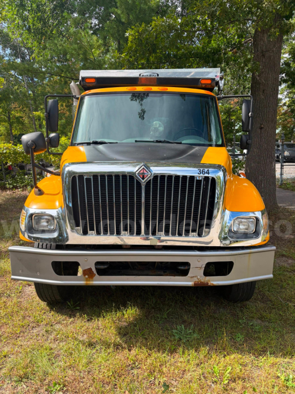 Front view of an orange 2005 International 7300 dump truck with chrome grille, headlights, and emblem, wind deflector, and bumper showing slight rust.