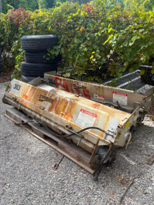 Dump trailer with rusted metal sides and warning labels, stacked with spare tires in background.