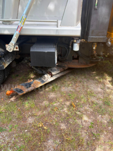 Rear-right side of a 2005 International 7300 dump truck showing a black plastic toolbox and hydraulic components near the undercarriage.