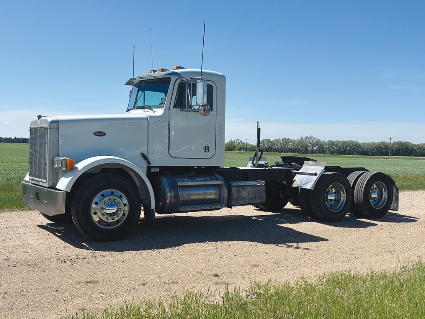Peterbilt 378 conventional daycab tractor in light gray, side view, with dual rear axles and chassis exposed, on dirt lot.