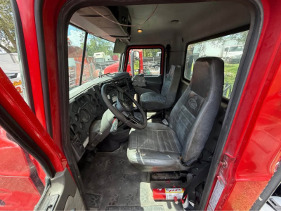 Truck cab interior of a red Mack CXU613 showing driver's seat, steering wheel, and passenger seat with dashboard and controls visible.