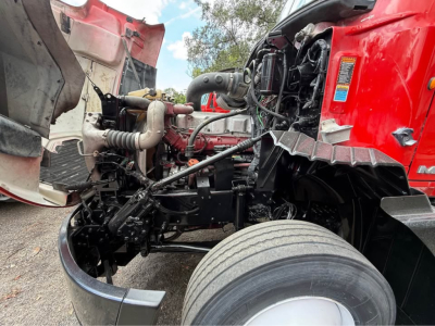Truck cab front view showing engine bay and exposed front suspension on a red Mack CXU613 with large front tire.
