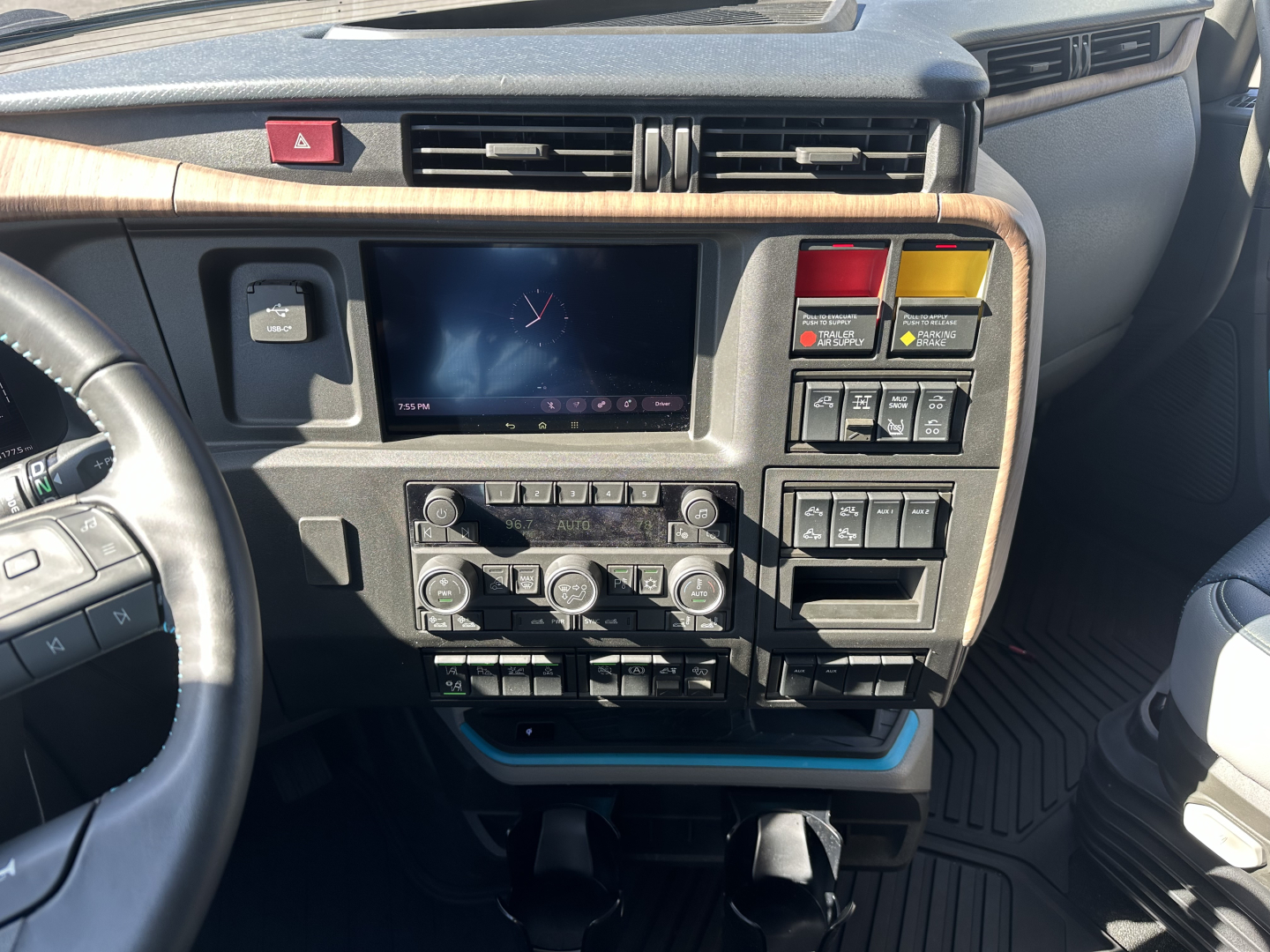 Volvo VNL64T860 dash area showing center touchscreen, climate controls, and various switches; woodgrain dash trim and steering wheel on left.
