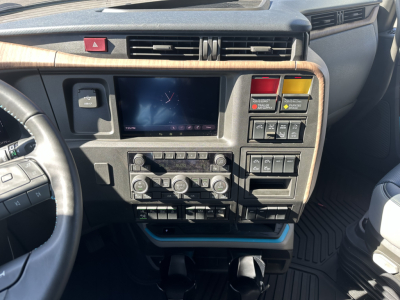 Volvo VNL64T860 dash area showing center touchscreen, climate controls, and various switches; woodgrain dash trim and steering wheel on left.