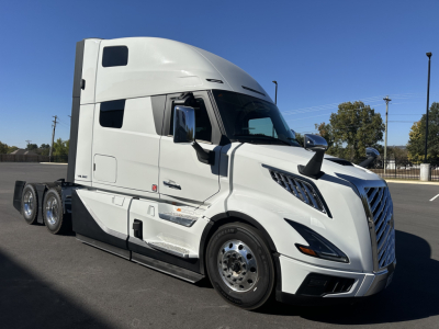 Volvo VNL64T860 sleeper cab truck in white, side view showing aerodynamic front, large chrome grille, 3-axle configuration, and side fuel tanks.