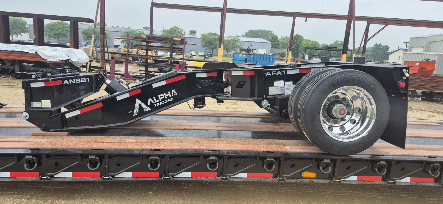Trailer spreader bar labeled ANSB1 Nitro spreading bar on a lowboy trailer showing Alpha branding and tires.