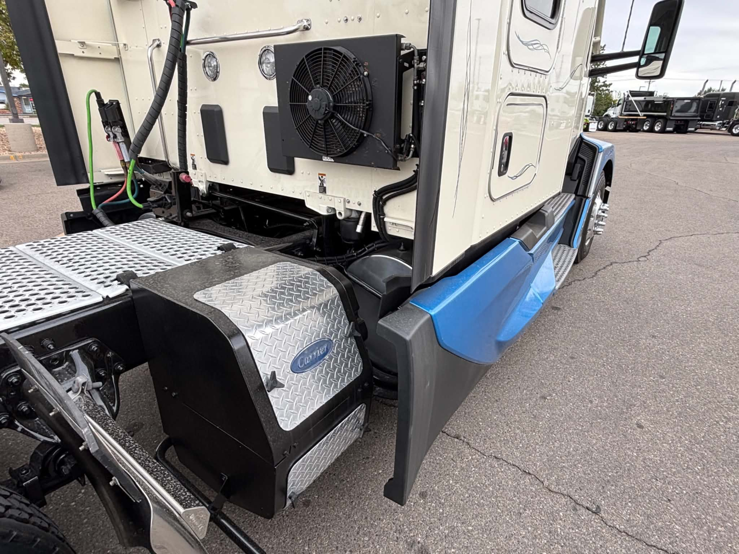 Kenworth T680 truck cab corner showing auxiliary coolant condenser and aluminum step plate with diamond plate texture near chassis.