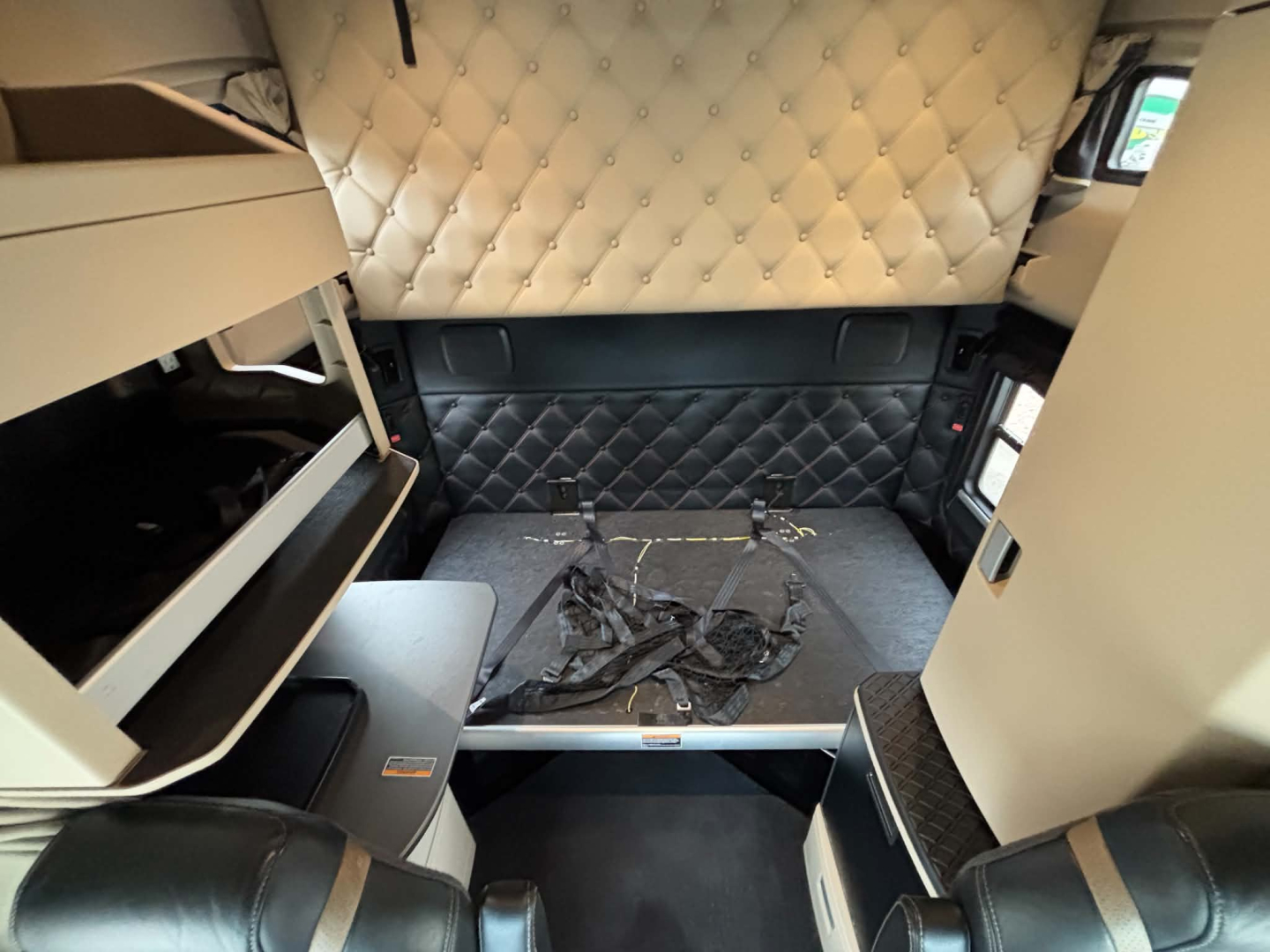 Kenworth T680 cab interior showing quilted light-colored upper sleeper panel and dark lower side walls with bunk area and straps.