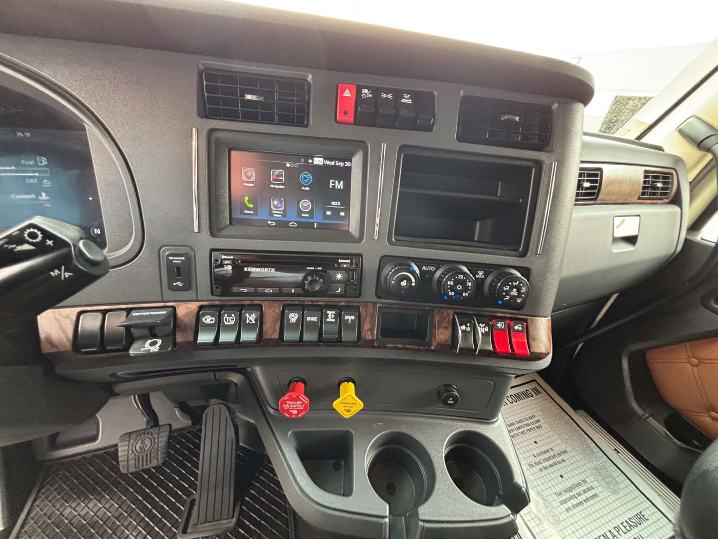 Kenworth T680 dash and center console showing infotainment screen, climate controls, and arrangement of switches.