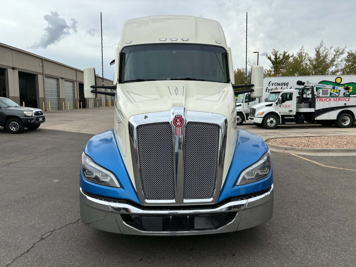 Kenworth T680 truck front view showing blue fenders, large chrome grille, and Kenworth emblem. Headlights visible with cab in light color.
