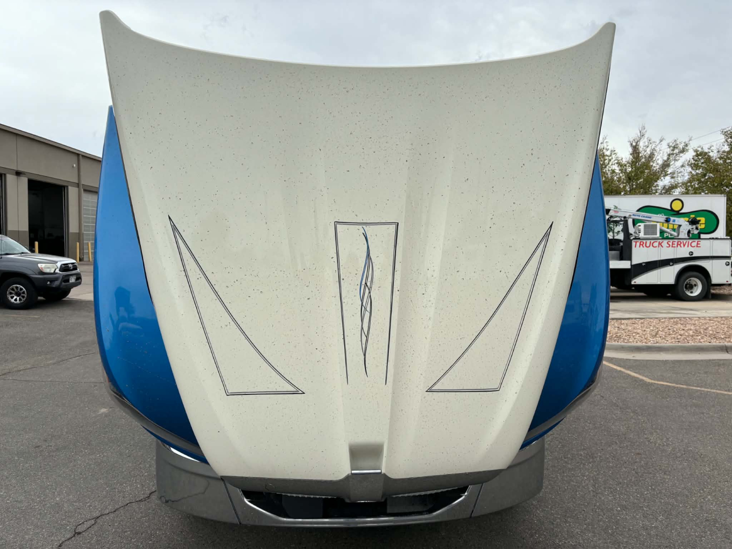 Truck hood of a 2024 Kenworth T680 with split hood design, white center with blue fenders, visible front of the cab.
