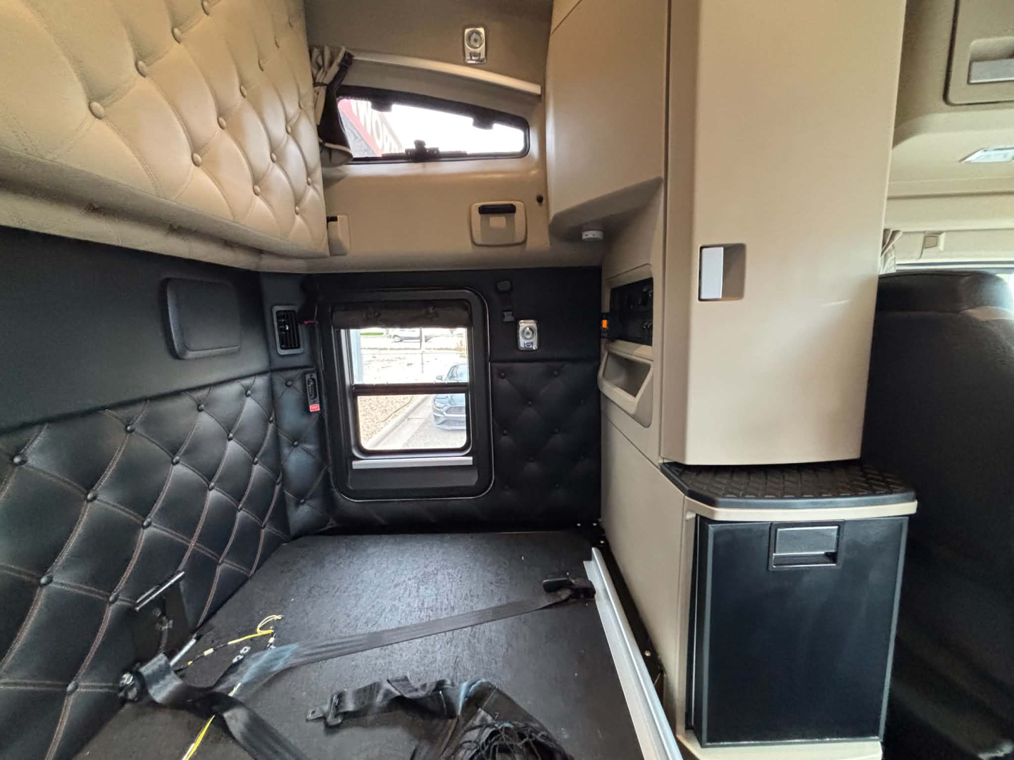 Kenworth T680 sleeper cab interior side view with quilted leather panels, window, and storage cabinet.