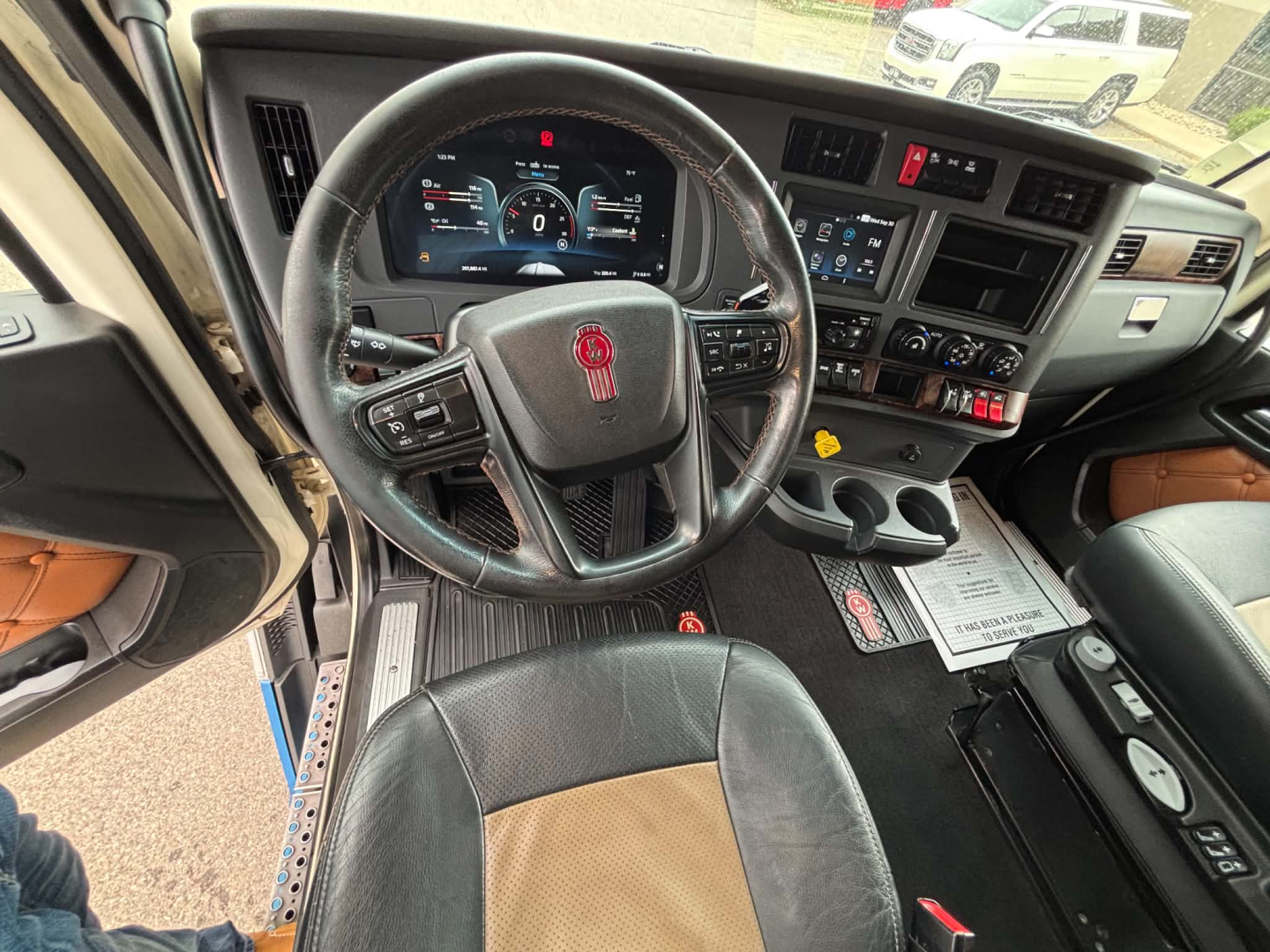 Truck interior dashboard and steering wheel of a 2024 Kenworth T680 with digital instrument cluster and center console.