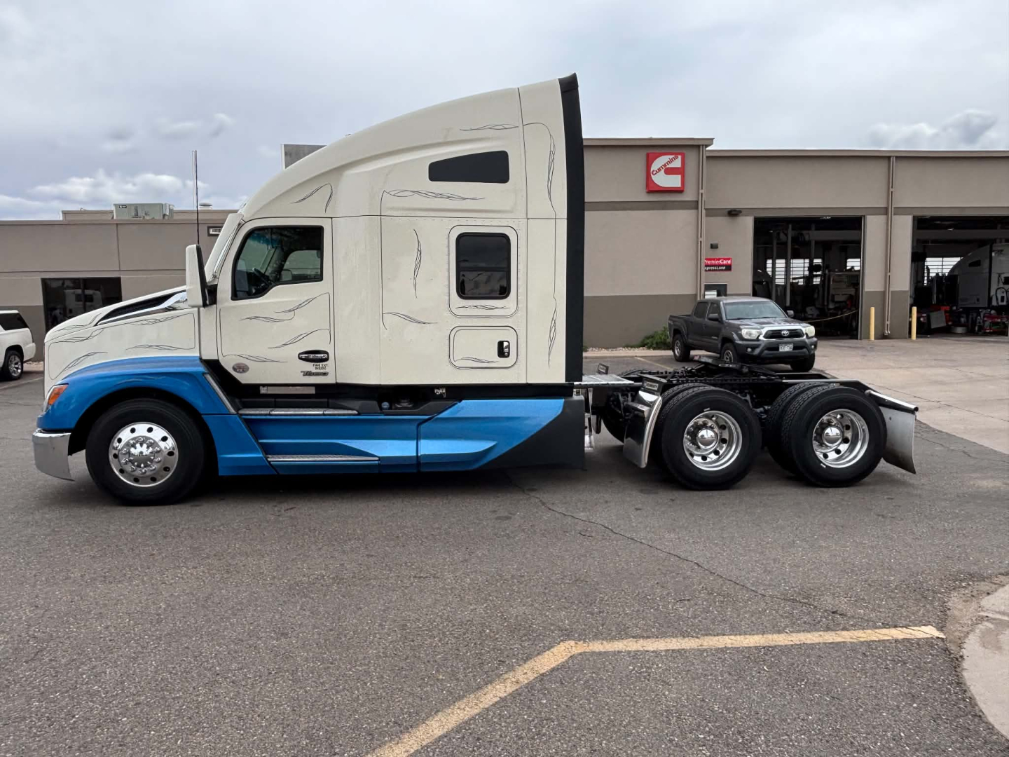 Kenworth T680 tractor with sleeper cab, side view showing two-tone white and blue paint, nozzle and wheel area.