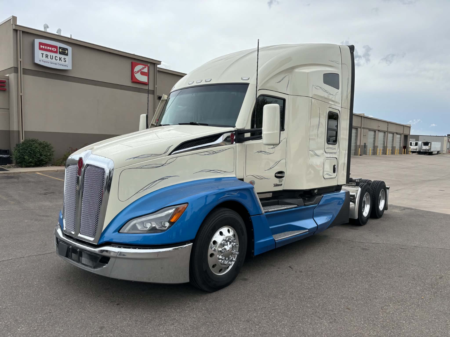 Kenworth T680 tractor in two-tone blue and white, side view showing sleeper cab, chrome front grille, and dual rear axle configuration.